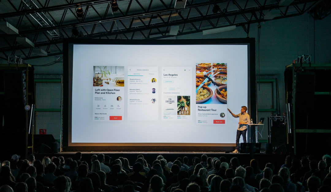 Man on stage in front of screen, presenting a pitch deck.